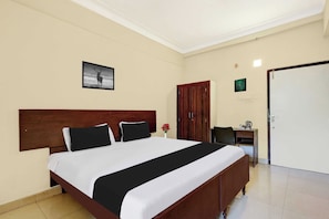 Quarto de hotel com uma cama grande, uma escrivaninha com cadeira, um guarda-roupa e uma porta.