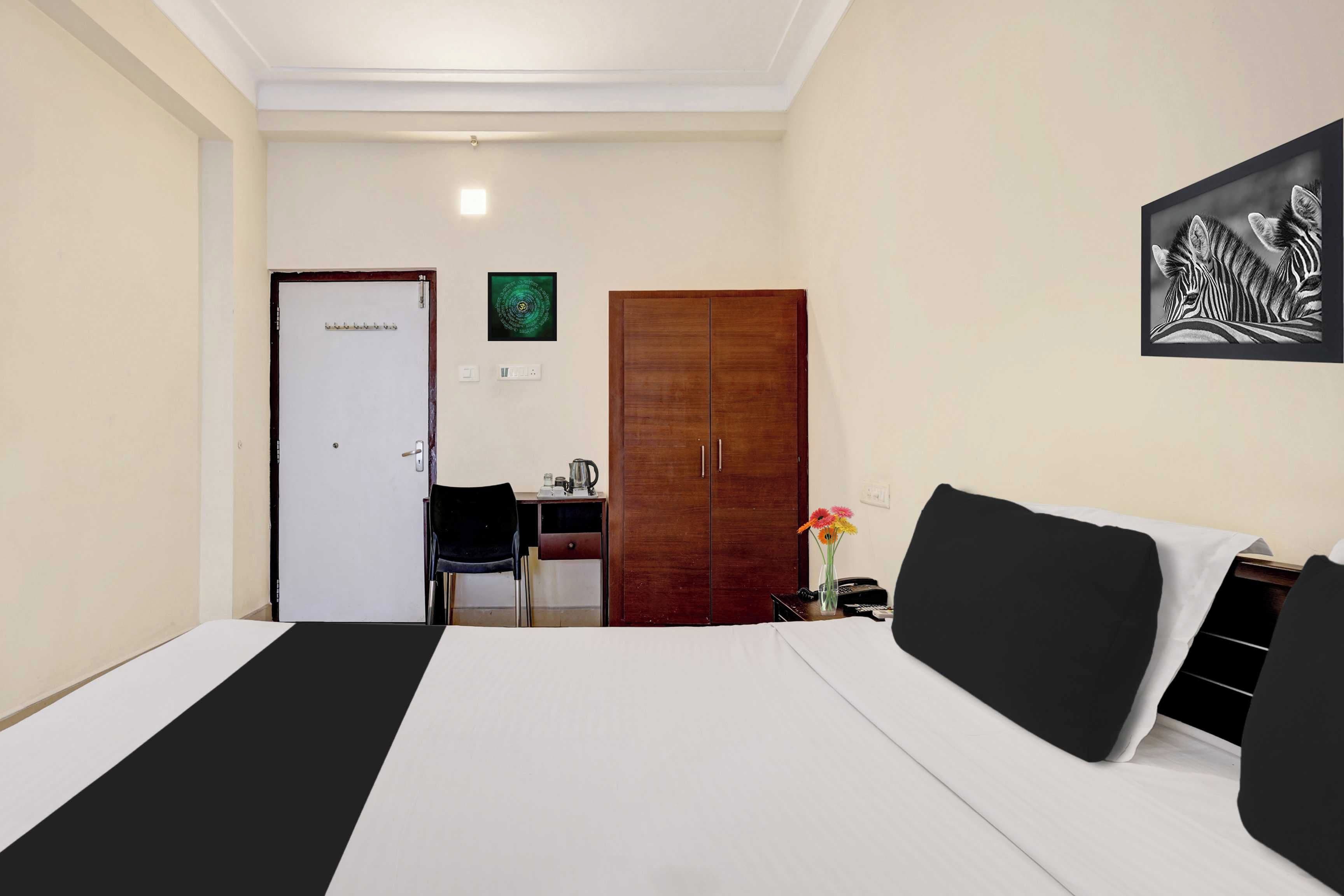 A hotel room with a bed, a desk, a chair, a wardrobe, and a wall-mounted artwork.