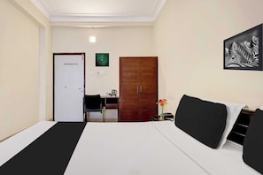 Quarto de hotel com cama, escrivaninha, cadeira, guarda-roupa e obra de arte pendurada na parede.