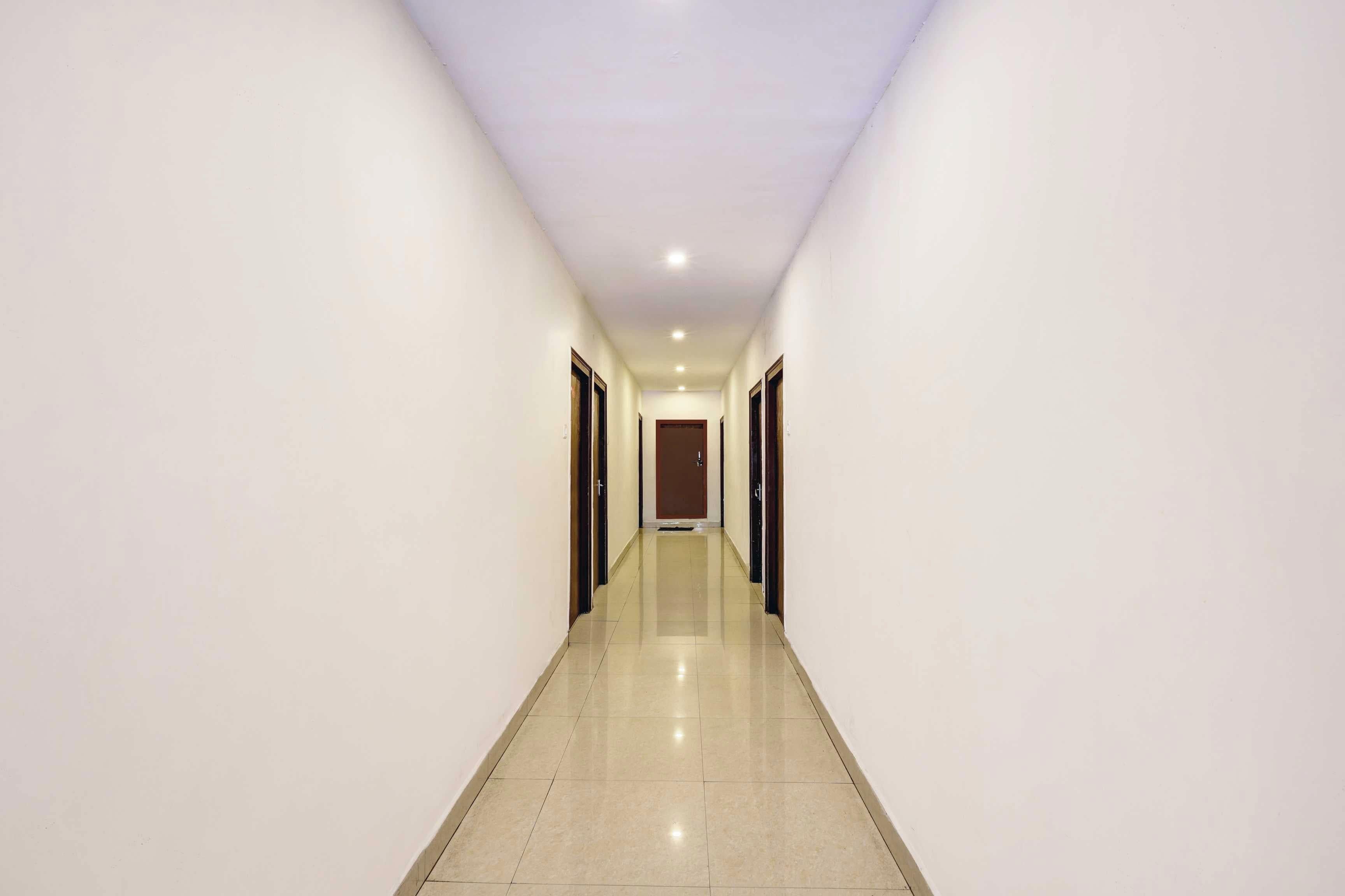 A long, narrow hallway with white walls and a shiny tiled floor, leading to a door at the end.