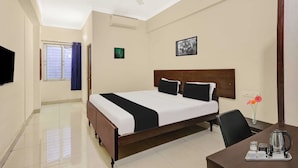 Habitación de hotel con cama, escritorio con hervidor, silla, ventana con cortinas y ventilador de techo.