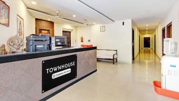 A reception desk with a sign indicating it's a company service area, a water dispenser, a bench, and a hallway leading to other rooms.
