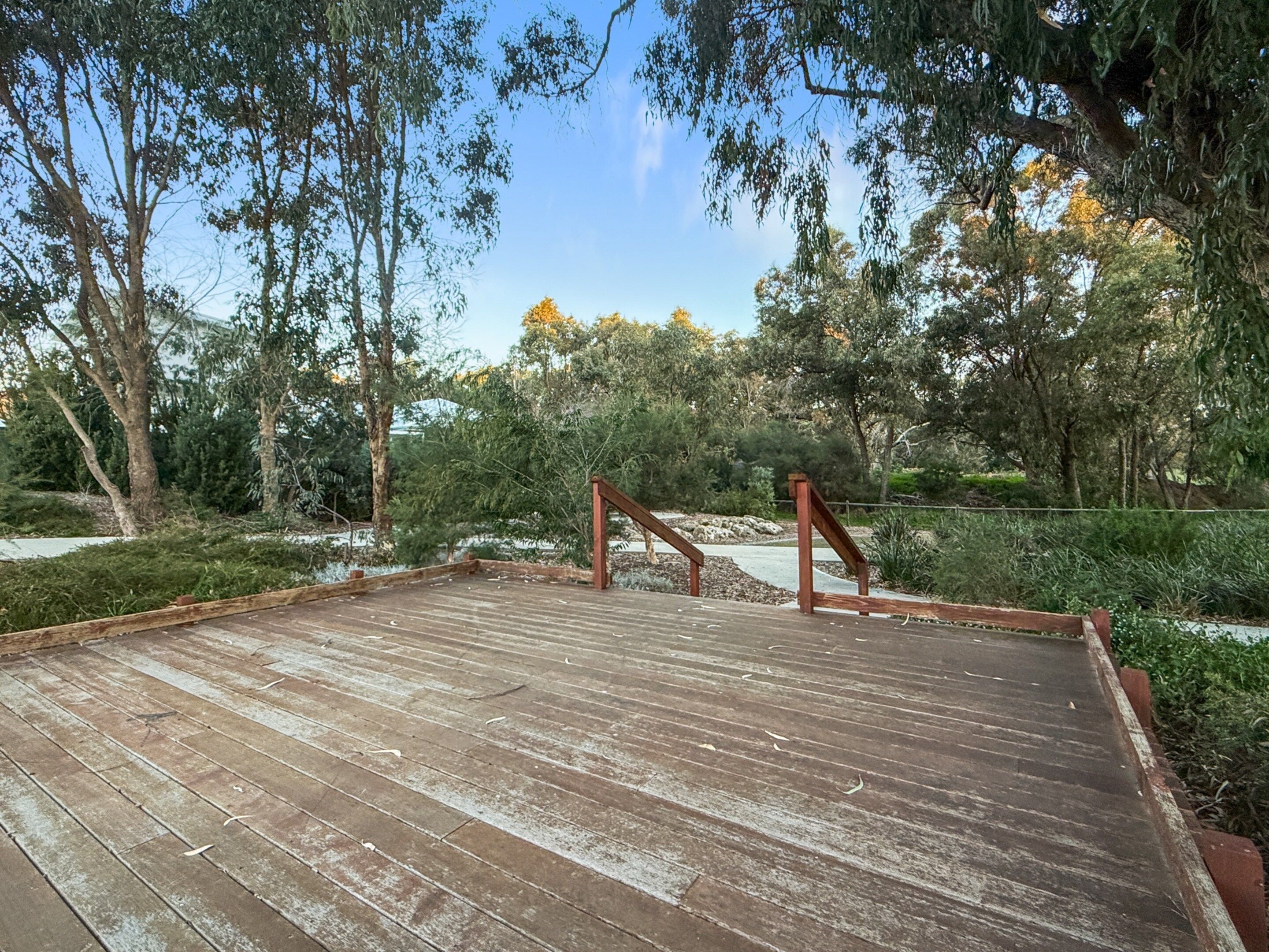 A wooden deck with metal railings, surrounded by trees and shrubs.