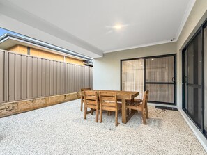 A room with a wooden table and chairs, a sliding glass door, and a view of a building outside. - Spacious 4-bed Retreat Near Meadow Springs (Perth)