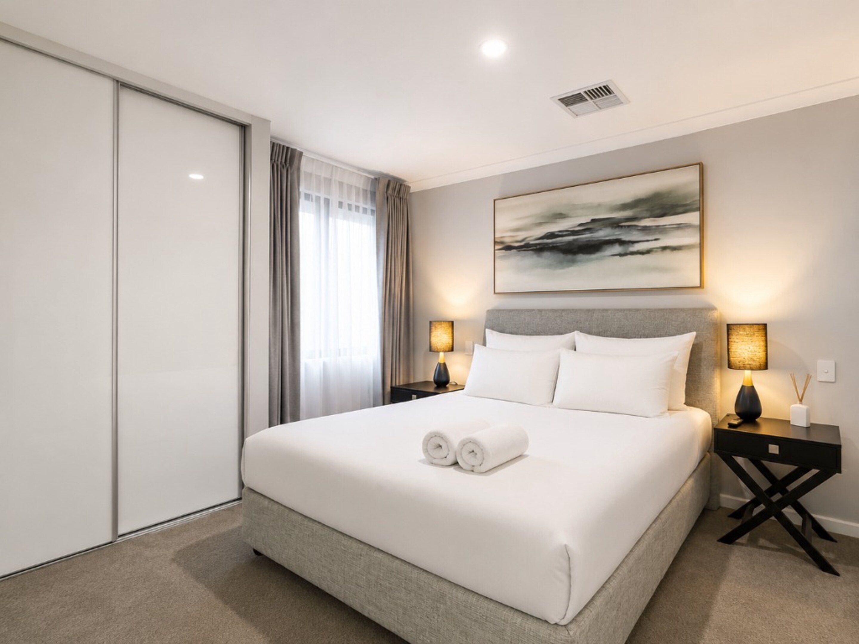 A hotel room with a large bed, two bedside tables with lamps, a painting on the wall, and a sliding door.