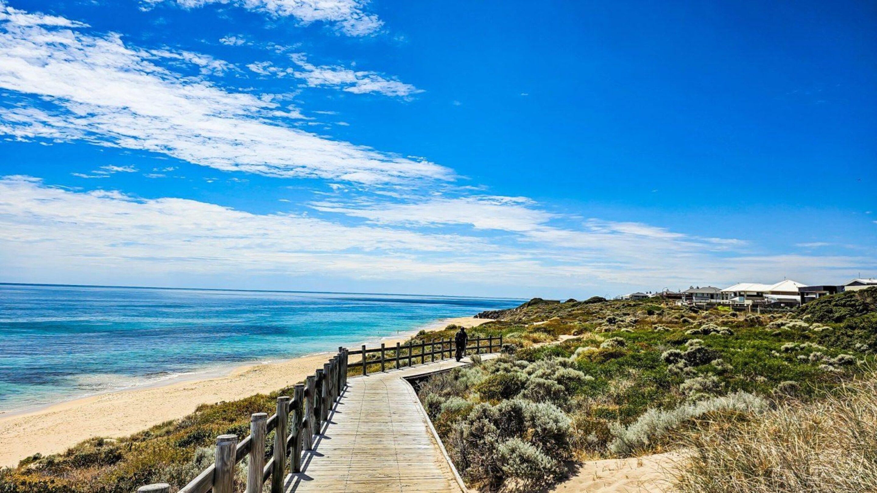A wooden boardwalk leading to a beach with clear blue water and a sandy shore.