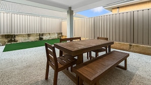 Eine Terrasse im Freien mit einem Holztisch und Stühlen, umgeben von einem hohen Zaun.