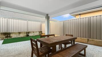 An outdoor patio with a wooden table and chairs, surrounded by a high fence.