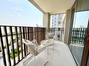 Ein Balkon mit Glastür, zwei Korbstühlen und einem kleinen Tisch mit einer Vase.