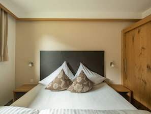 A bedroom with a large bed, two nightstands, a wooden headboard, and a wall-mounted lamp. - Haus am Brunnen, (Samnaun-Compatsch) by Interhome (Samnaun)