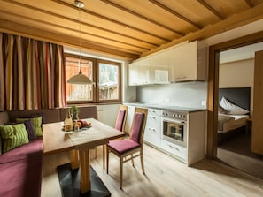 A cozy kitchen with wooden beams, a dining table with chairs, and a view of a bedroom. - Haus am Brunnen, (Samnaun-Compatsch) by Interhome (Samnaun)