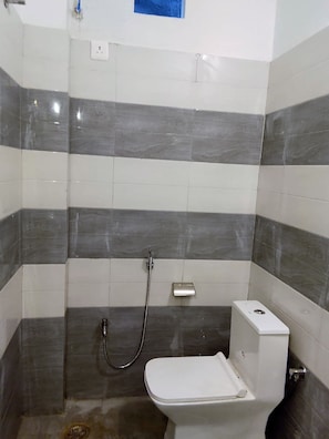 A bathroom with a shower, toilet, and a wall-mounted faucet. - Shivansi Residency (Varanasi)