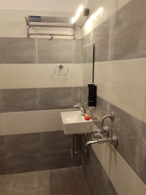 A bathroom with a white sink, a handheld showerhead, and a towel rack. - Shivansi Residency (Varanasi)