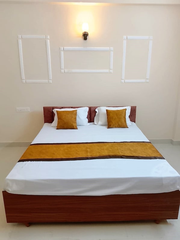 A bed with a wooden frame, white bedding, and two brown pillows. - Shivansi Residency (Varanasi)