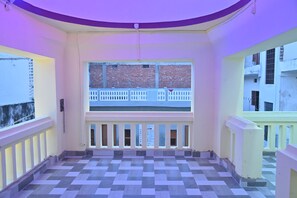 A corridor with a checkered floor, a balcony with a white railing, and a view of a brick building.