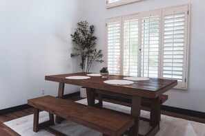 A dining table with a bench, a potted plant, and a window with blinds. - Vegas Gem Retreat w/Pool & Nearby Strip (Henderson)