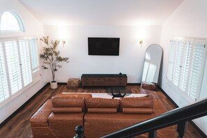 A modern living room with a brown leather sofa, a wooden cabinet, a flat-screen TV, and a large mirror. - Vegas Gem Retreat w/Pool & Nearby Strip (Henderson)