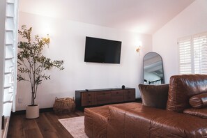 Een kamer met een bruine leren bank, een houten kast, een grote spiegel en een kamerplant.