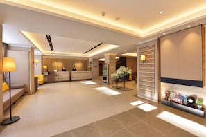 Eine moderne Hotelhalle mit einer Rezeption, einer Sitzecke und einer Wanddekoration mit einer Uhr und Figuren.