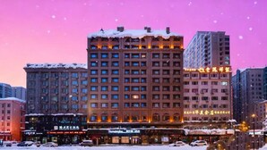 Um hotel com vários andares, teto coberto de neve, janelas iluminadas e uma placa visível em língua estrangeira.