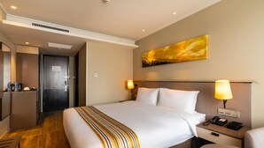 Quarto de hotel com cama, mesa de cabeceira, abajur e um quadro na parede.
