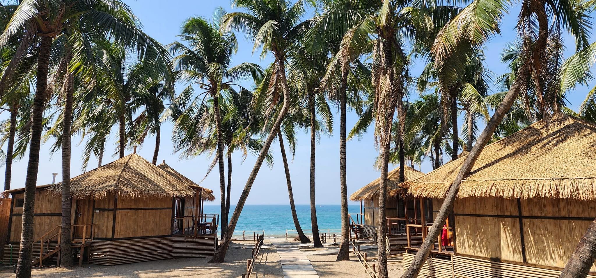 Ein Strand mit strohgedeckten Hütten und Palmen.