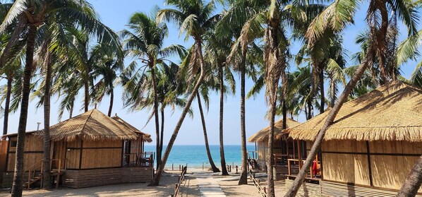 A beach with thatched-roof huts and palm trees.