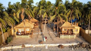 Un resort con bungalós de techo de paja, una playa de arena y palmeras.