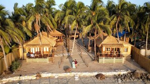 Een resort met bungalows met rieten daken, een zandstrand en palmbomen.