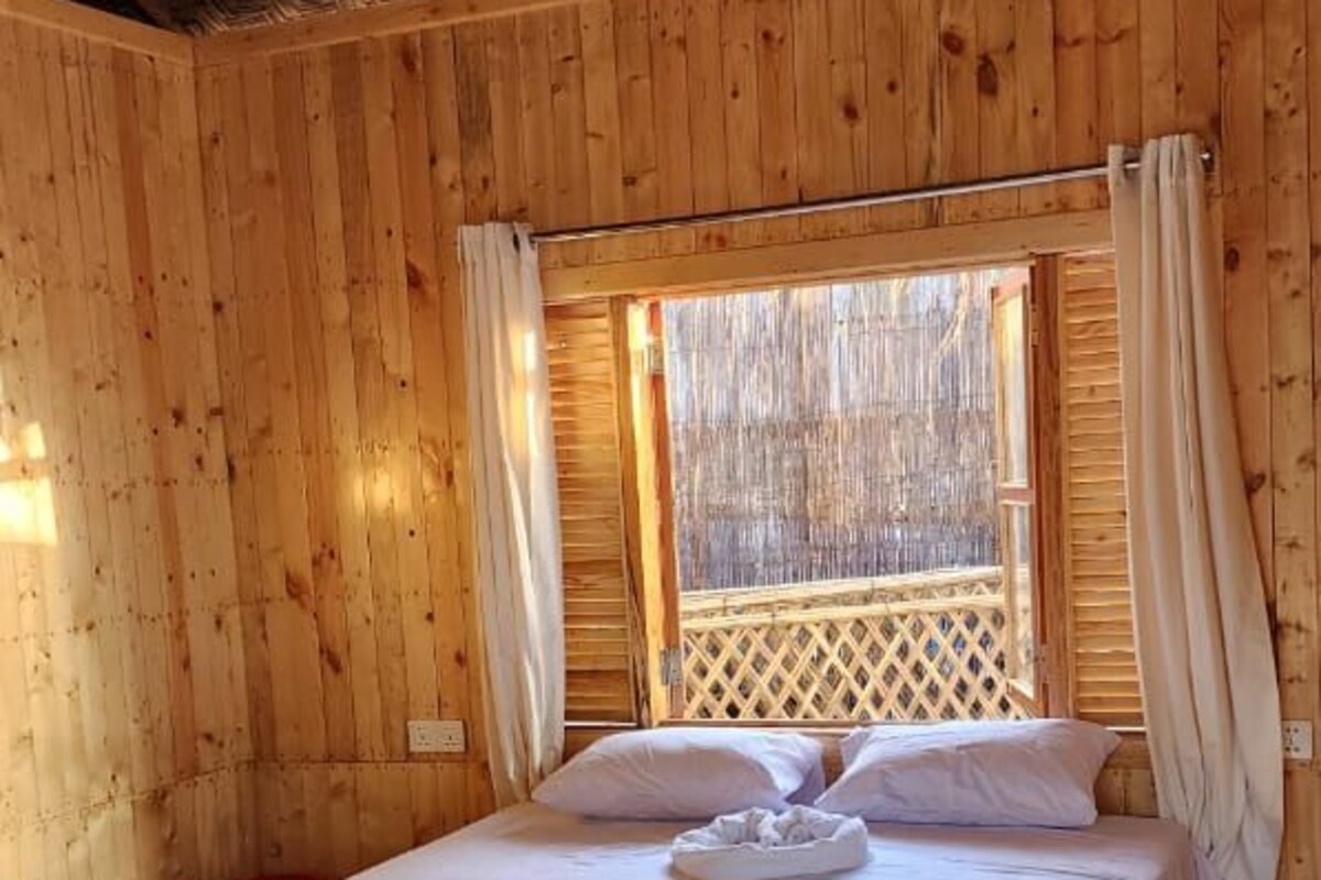 A wooden room with a bed, a ceiling fan, and a window with curtains.