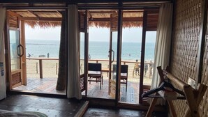 Una habitación con un gran ventanal corredero que da a una terraza de madera con vistas a la playa.