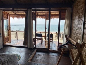 Een kamer met een grote schuifdeur die uitkomt op een houten terras met uitzicht op het strand.