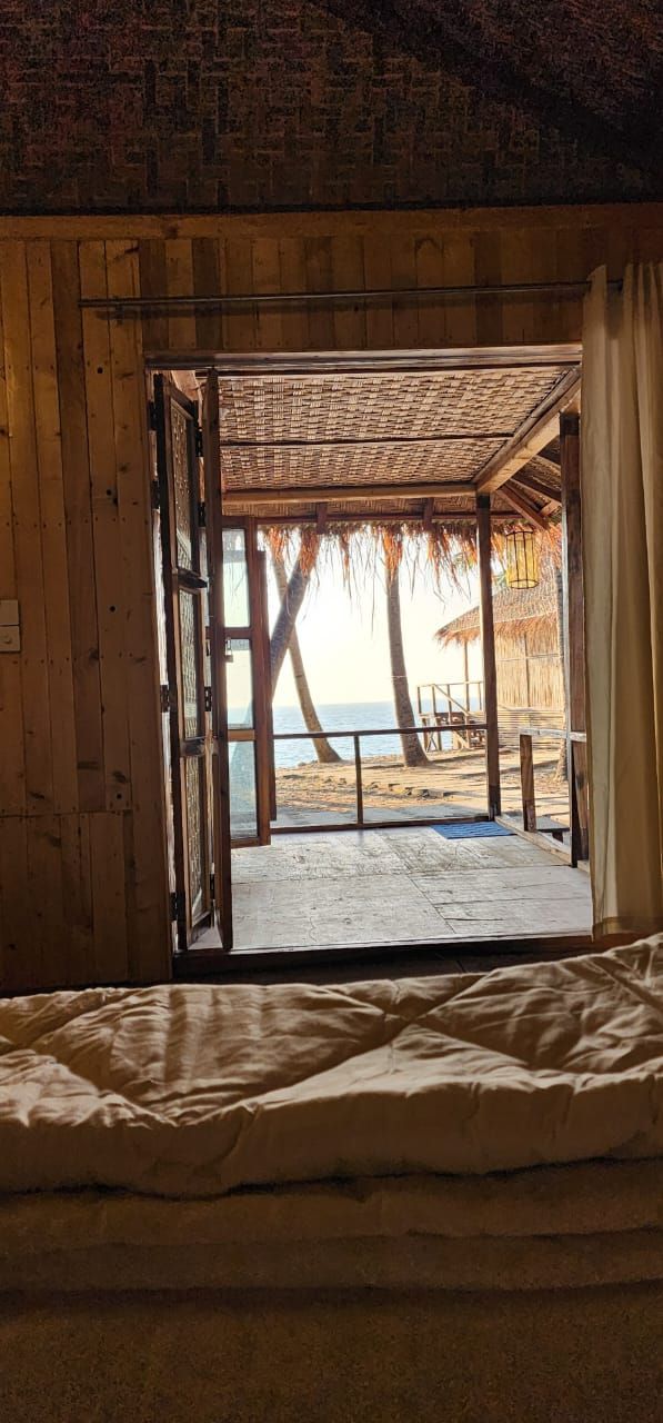 Une porte en bois ouverte donnant sur une vue de la plage, avec une structure surmontée d’un toit de chaume.