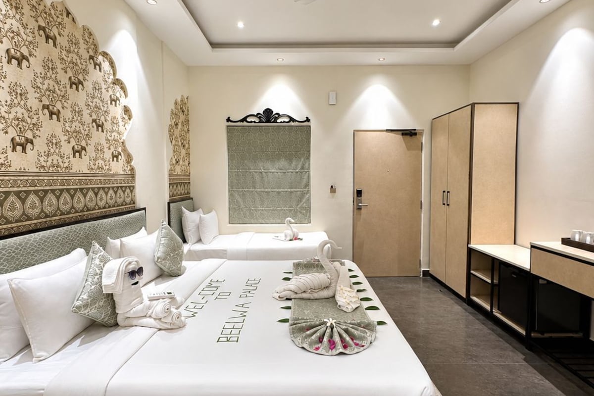 Habitación de hotel con dos camas, un armario, un escritorio y un ventilador de techo.