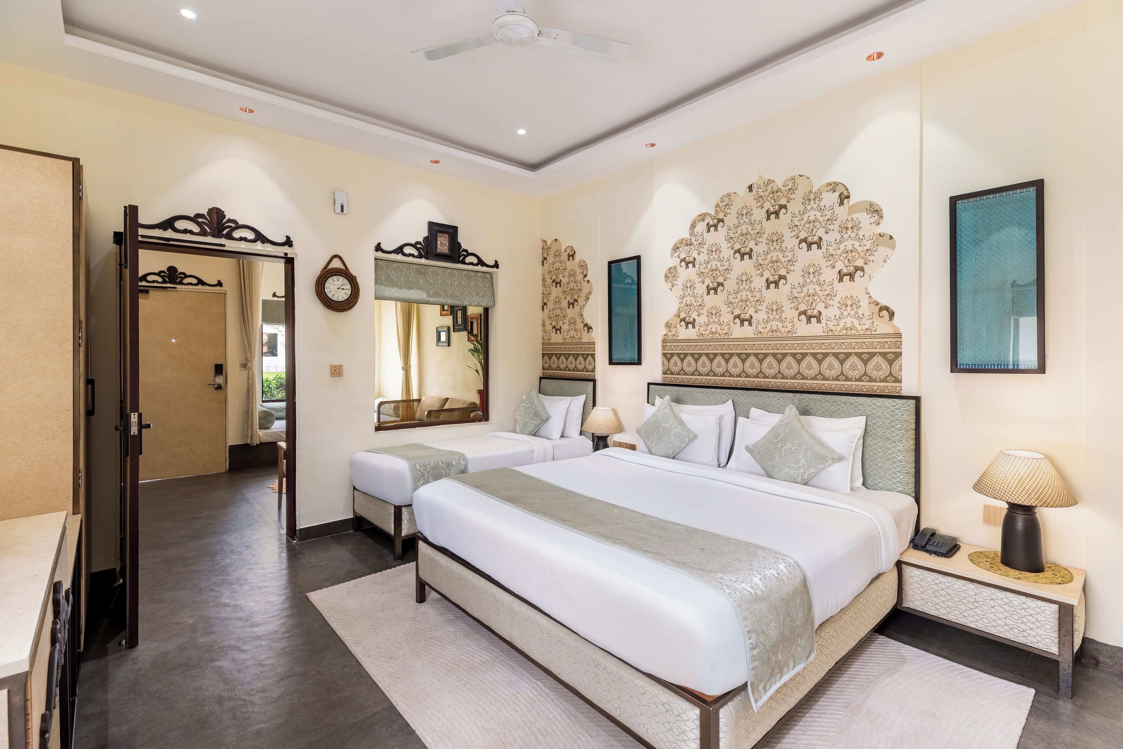Una habitación de hotel con una cama grande, dos mesitas de noche, un tocador, un espejo y un cabecero decorativo.