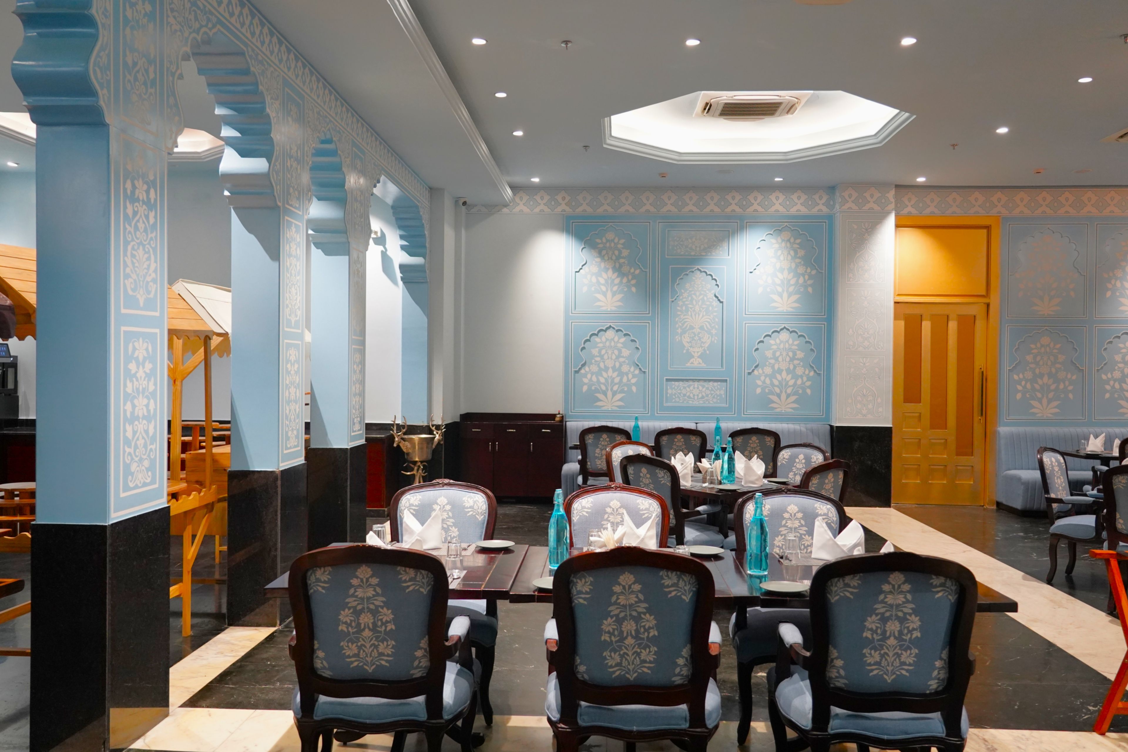 A dining area with tables and chairs, a ceiling with recessed lighting, and decorative wall panels.