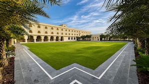 A courtyard with a central lawn, surrounded by a building with arched windows and a tiled walkway. - Beelwa Palace  (Jaipur)