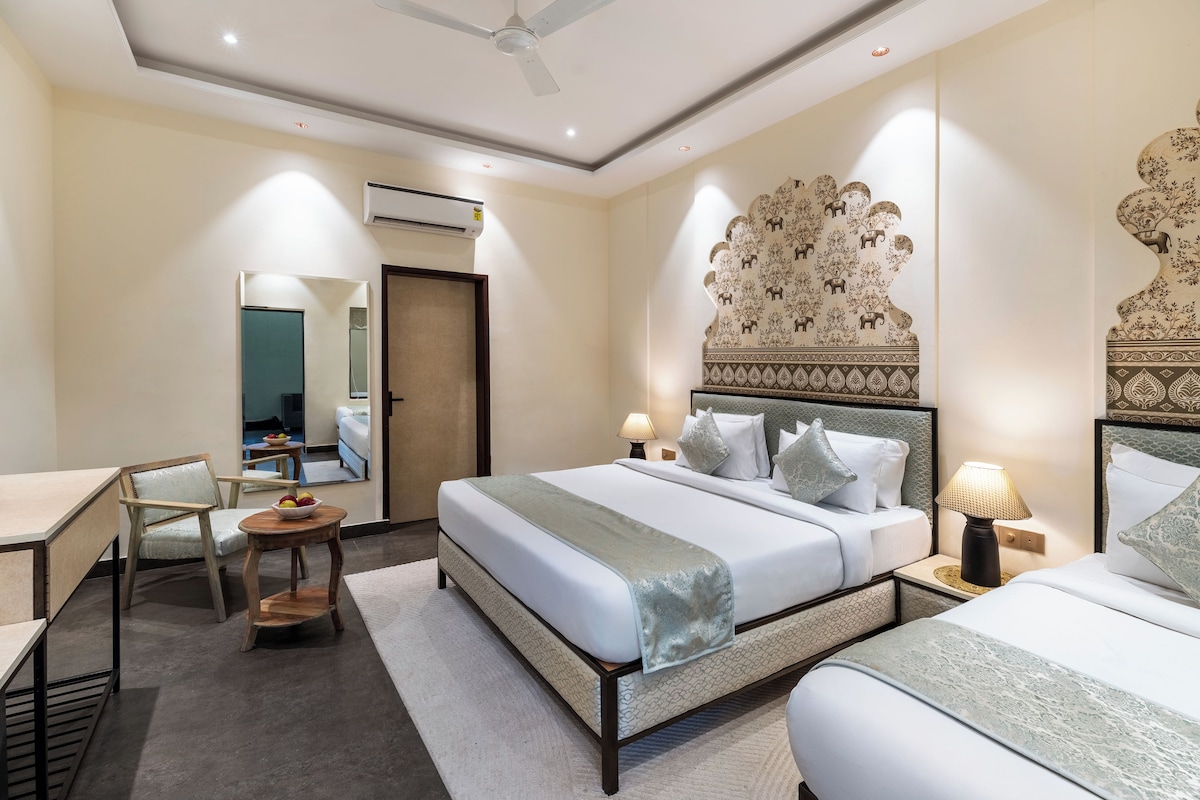 Habitación de hotel con cama, escritorio, silla, una pequeña mesa con fruta y espejo.