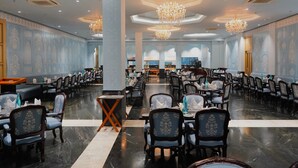 A spacious dining area with multiple tables and chairs, a central column, and decorative chandeliers. - Beelwa Palace  (Jaipur)
