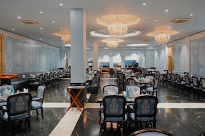 Un comedor amplio con varias mesas y sillas, una columna central y candelabros decorativos.