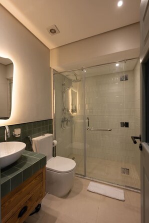 Ein modernes Badezimmer mit einer gläsernen Duschkabine, einer weißen Toilette und einem großen Waschbecken.