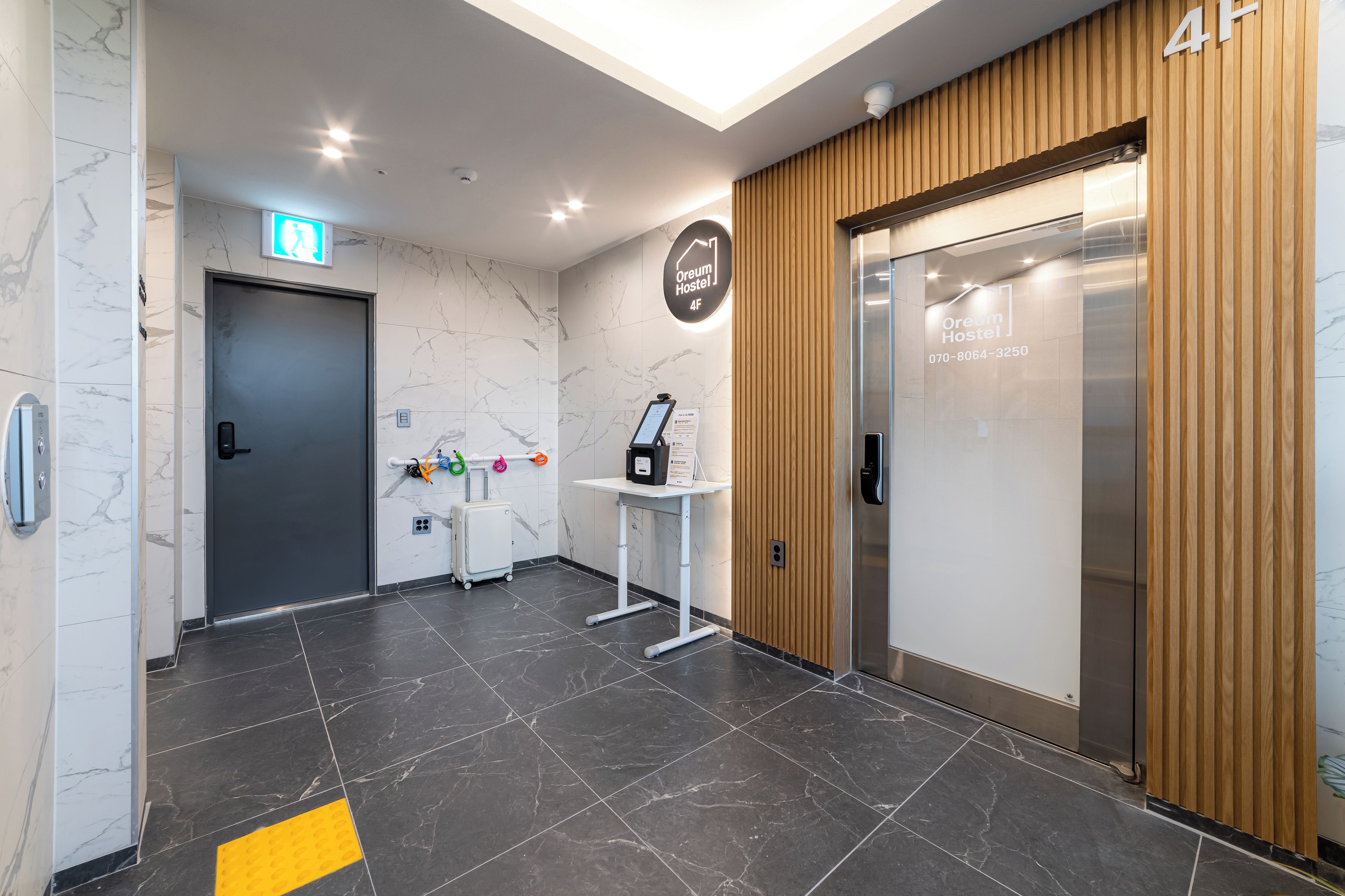 A modern hotel lobby with marble walls, a reception desk, a luggage trolley, and an elevator.