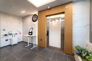 A hotel reception area with a marble wall, a wooden panel, a reception desk, and a luggage trolley. - Oreum Hotel Dongdaemun (Seoul)