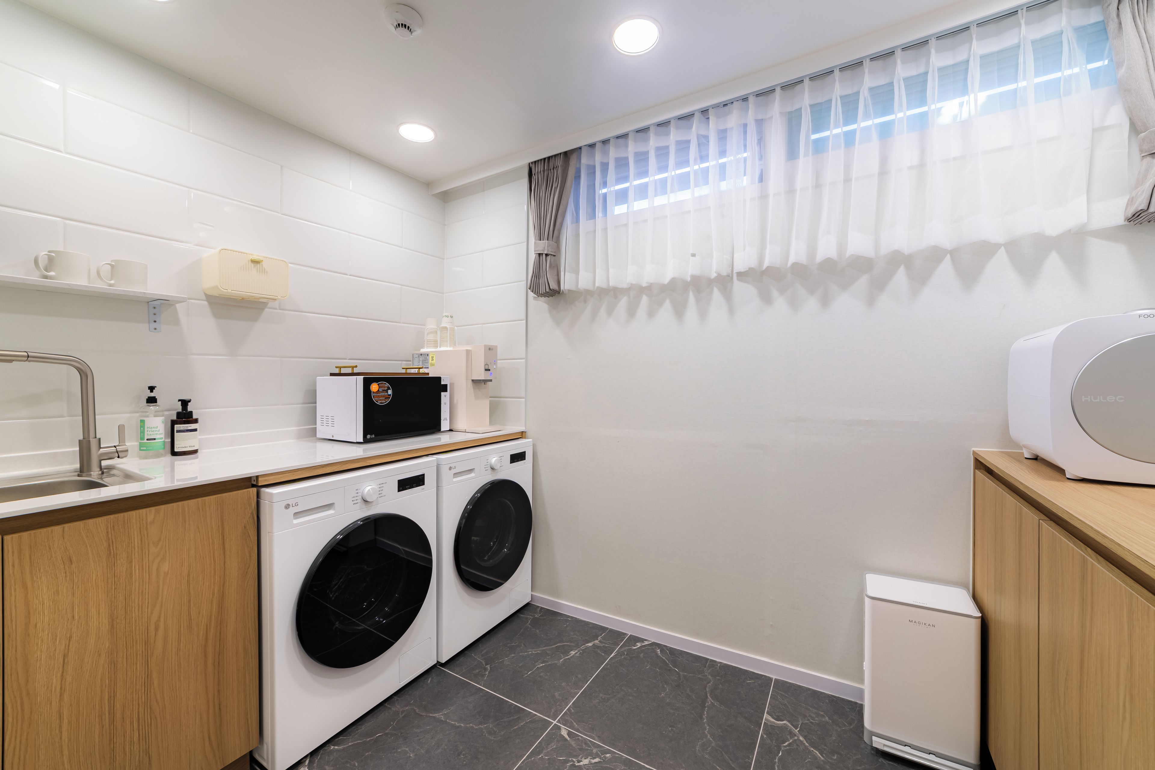 A compact laundry room with two front-loading washing machines, a small sink, and a microwave on a wooden countertop.