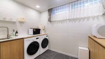A compact laundry room with two front-loading washing machines, a small sink, and a microwave on a wooden countertop.