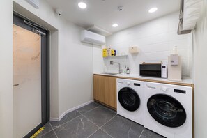 A compact laundry room with a washing machine, dryer, microwave, and a small shelf with toiletries. - Oreum Hotel Dongdaemun (Seoul)
