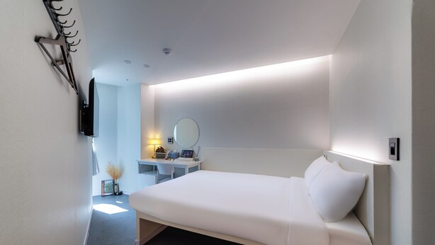 Una habitación de hotel moderna con una cama, un escritorio, una silla, un espejo y un televisor.