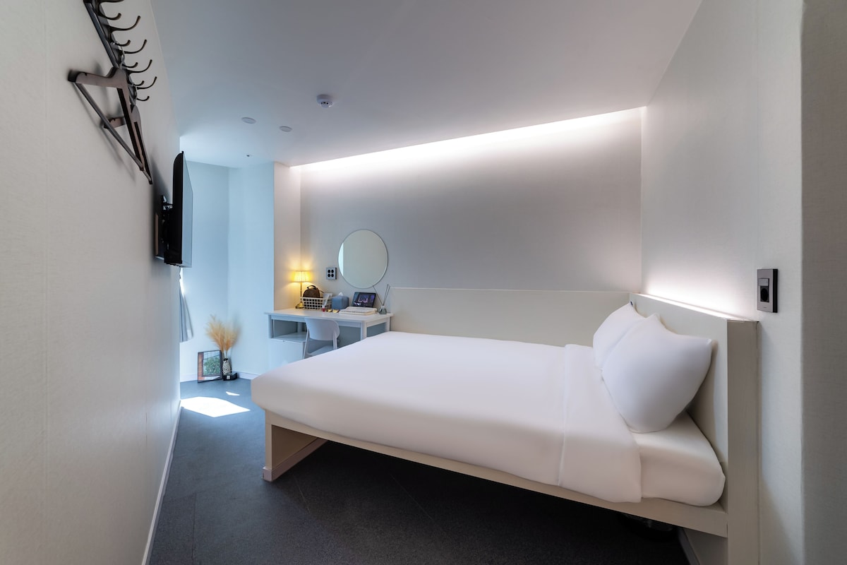Une chambre d’hôtel moderne équipée d’un lit, d’un bureau, d’une chaise, d’un miroir et d’une télévision.