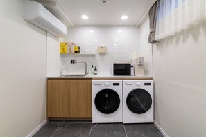 Une petite buanderie comprenant un lave-linge, un sèche-linge, un four à micro-ondes et une petite étagère avec quelques articles.