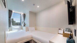 Habitación de hotel con cama, escritorio, televisor y ventana con cortinas.